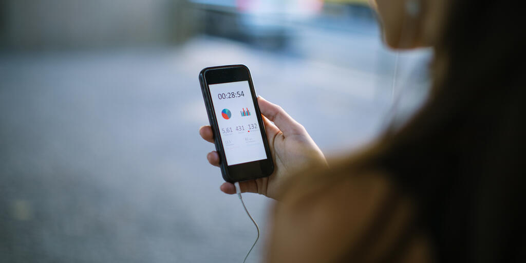 Close up of woman holding smart phone and using fitness app to check her training progress.